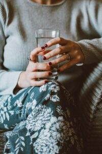 Person Sitting on Grey Sofa While Holding Clear Highball Glass of Water